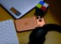 Laptop, phone, keyboard, headphones, and puzzle cube on desk.