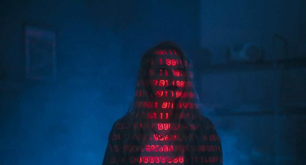 A mysterious silhouette with red binary code projected over the face, set against a dark, moody background.