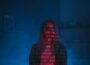 A mysterious silhouette with red binary code projected over the face, set against a dark, moody background.