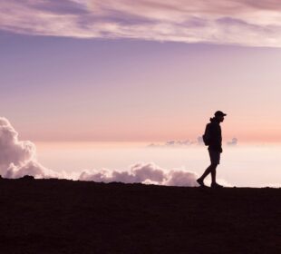 silhouette of person walking under white clouds