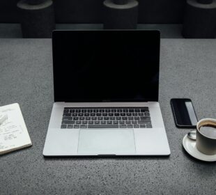 turned-off MacBook Pro between cup of coffee, iPhone, notebook, and pen