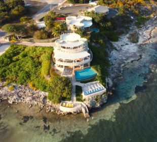 A stunning aerial view of a luxury villa on Grand Cayman with a seafront pool and lush greenery.