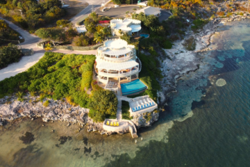 A stunning aerial view of a luxury villa on Grand Cayman with a seafront pool and lush greenery.